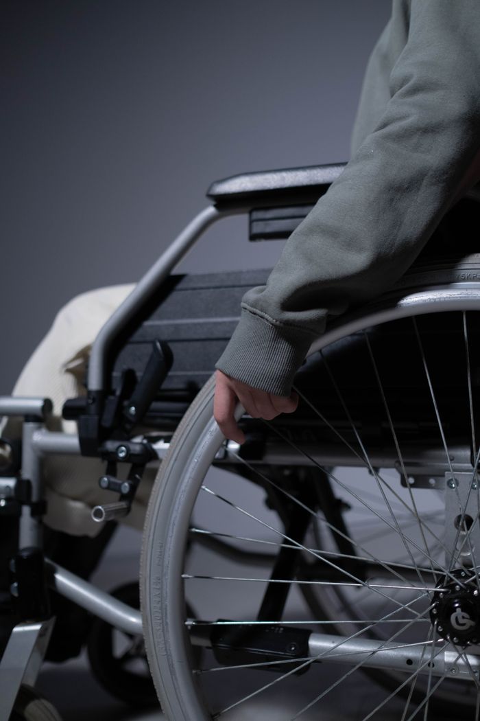 Home A detailed close-up shows a person's hand resting on a wheelchair rim, emphasizing disability and mobility aids.
